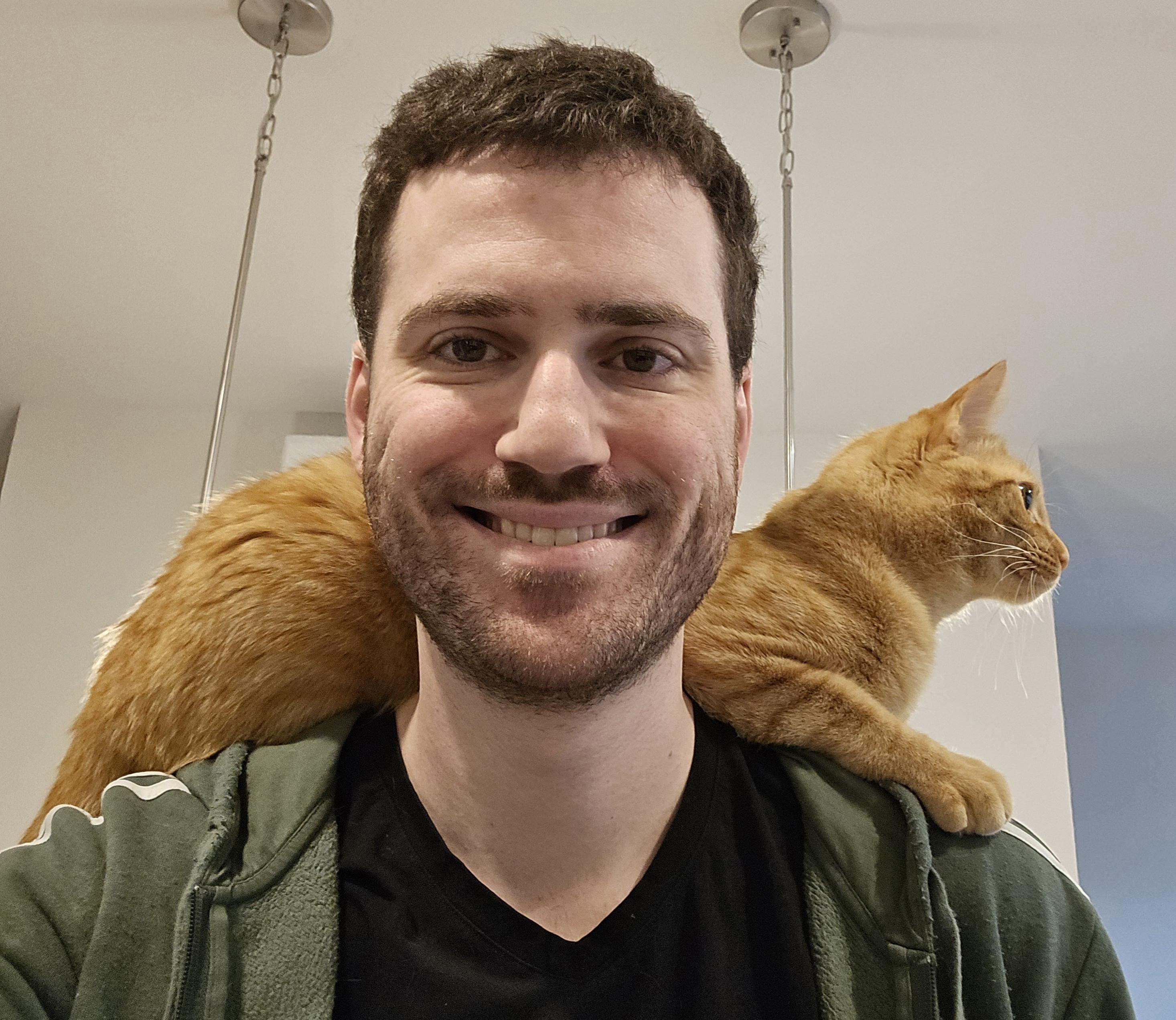 A selfie of a person with an orange tabby cat laying across their shoulders.