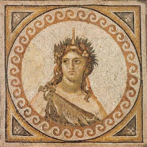 Mosaic of a bust of Dionysos inside a circle decorated with a band of wave patterns. The god is giving some serious side-eye while dressed in an animal skin tied over his right shoulder. His head is adorned with a crown, grape or ivy clusters, and long ribbons.