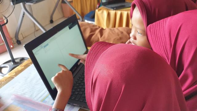 In einem indonesischen Klassenraum sitzen an mehreren Tischen Gruppen von Schülern und Schülerinnen vor aufgeklappten Laptops.
Auf den Bildschirmen sieht man das Programm Geogebra. Auf einer Leinwand vor den Schülern zeigt eine Folie eine Lektion zum Thema Kreis und Kreissegmente.
Alle Kinder lernen eifrig, diskutieren und zeigen teils mit dem Finger auf den Monitor.