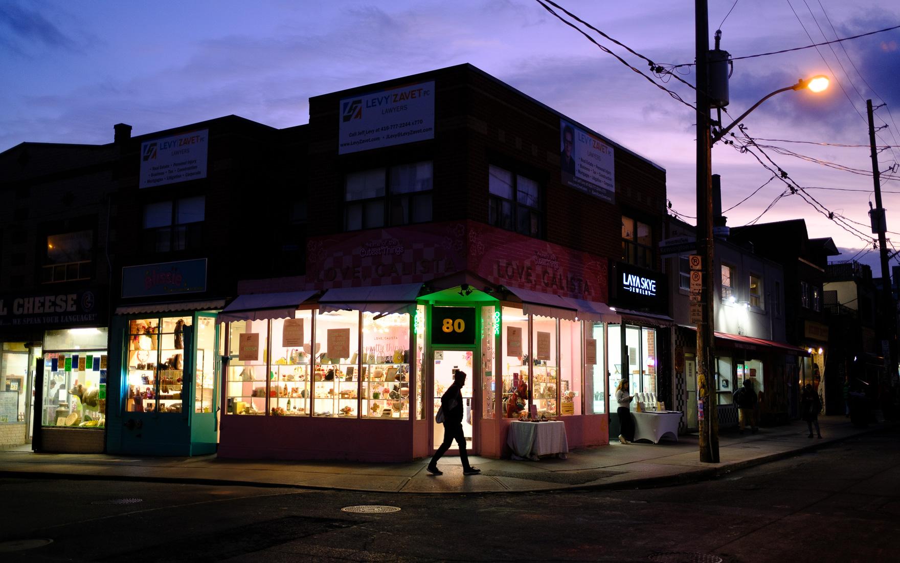 a woman walks by the entry of a brightly lit store at 5:15pm, about 20 minutes after sunset on the corner of Kensington and Baldwin in Toronto. Taken with a Fuji x100vi, November 14 2025