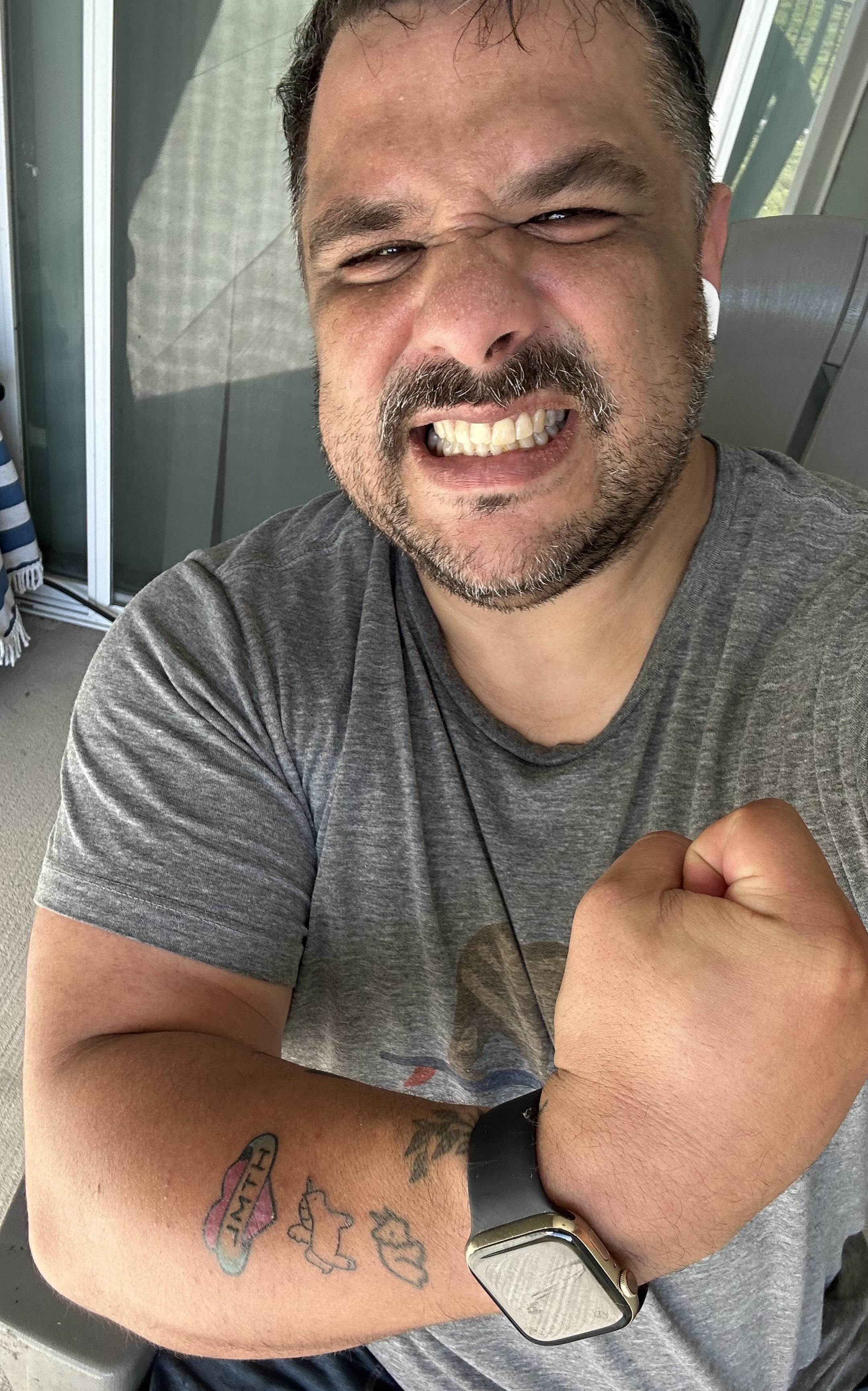 Me, sweaty. Trying to flex my muscle. Vaguely succeeding. Wearing a gray t-shirt.  