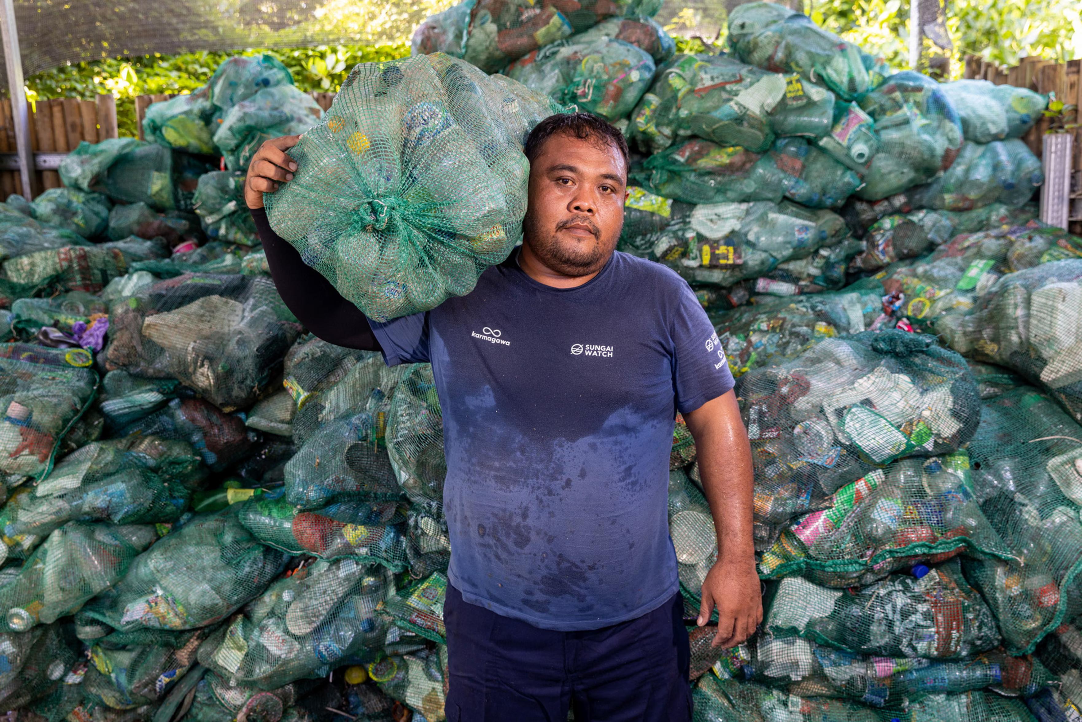 A man holds up bags of plastic water bottles at a recycling centre.