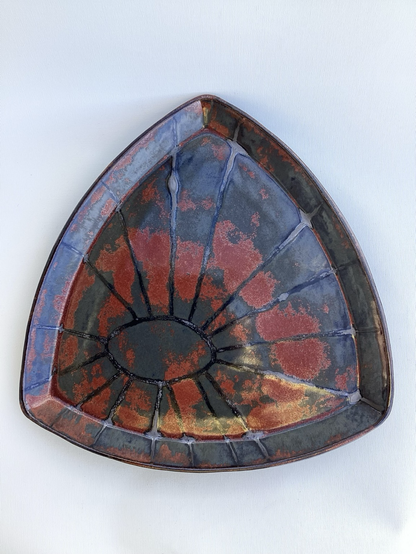 Größerer dreieckiger Teller mit rot, schwarz, grauer Glasur und einem ovalen Kreis in der linken unteren Hälfte, von dem Strahlen ausgehen 