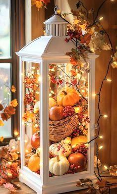 A beautiful white framed vintage looking lamp used as a decoration filled with autumn things and adorned with tiny lights 