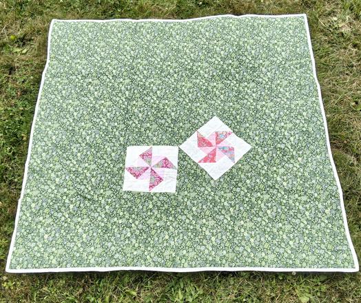 the reverse side of the quilt, it is green with small flowers on it, sewn into the back are two off-center pinwheel designs on white squares 