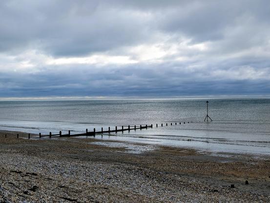 Shingle beach at low tide, with a calm sea and moody grey skies