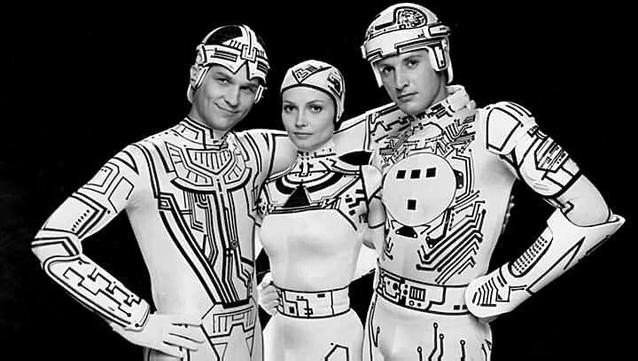 Black-and-white production shot from the set of Tron from 1982 showing Jeff Bridges, Cindy Morgan, and Bruce Boxleitner in their black-and-white outfits on the set