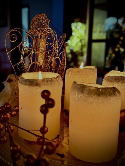 4 leuchtende Kerzen auf einem Adventskranz mit einem Engel im Hintergrund