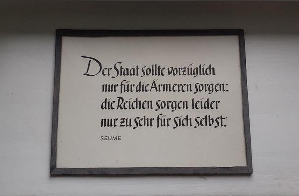Bilderrahmen in einer Ausstellung mit dem Text: 
"Der Staat sollte vorzüglich nur für die Ärmeren sorgen: die Reichen sorgen leider nur zu sehr für sich selbst. "
Seume