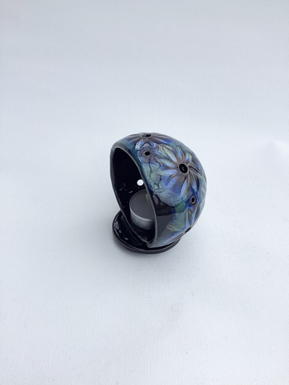 Stehende (etwas mehr als) Halbkugel mit eingeritzten Blättern um unterschiedlich große Löcher herum. Glasur: schwarz mit grün,blau und violett 