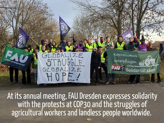 Gruppe von ca. 30 FAU-Gewerkschafter:innen die mit einem Banner "Globalize struggel - globalize hope", Fahnen und Westen vor einem herbstlichen Park posieren. 