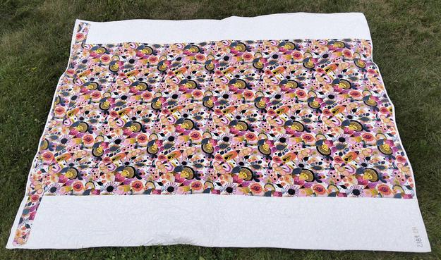 the reverse side of the quilt, it is bright colors of orange and white and yellow, a big rectangle, on a larger white backing, the ends of the left side extended further outwards 