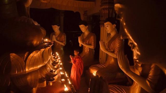 A small Buddhist monastic offering lamps to a Buddha statue.