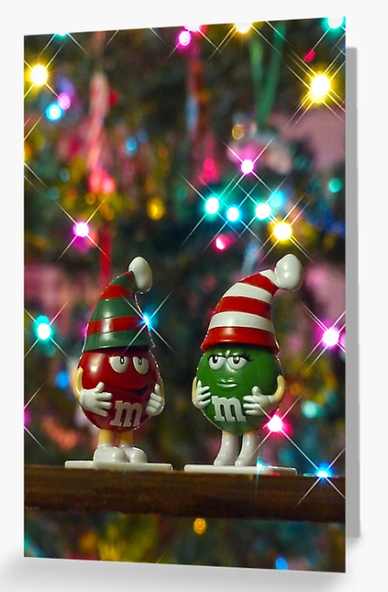 An adorable Christmas card with Mr. Red and Mrs. Green M&M with the sparkling lights of a Christmas tree in the background. 