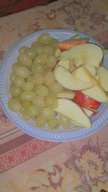 A plastic plate with white grapes and sliced red apple.