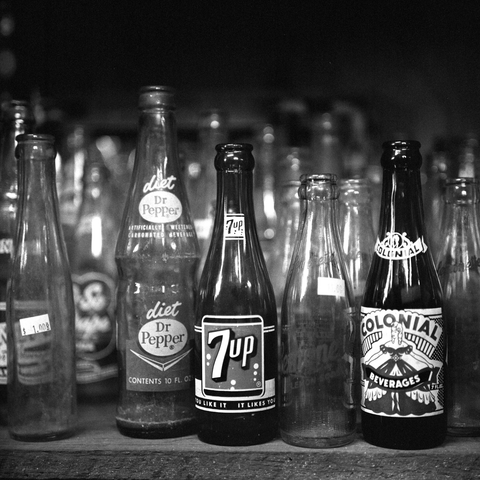 A black-and-white film photo. A collection of old soda bottles sit ready for sale at Broadway Paul’s Antiques & Salvage in Paige, Texas. Friday, November 7, 2025.