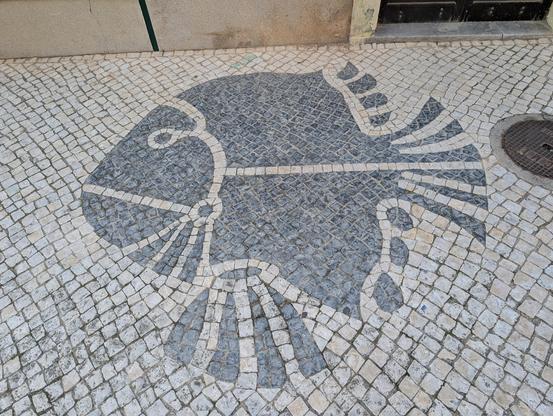 A design of a big flat fish in black paving stones, surrounded by small white paving stones. 