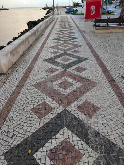 A geometric design of small and large squares rotated 45 degrees of the main axis, with the squares in brown or black stone and the surroundings in white stone. 