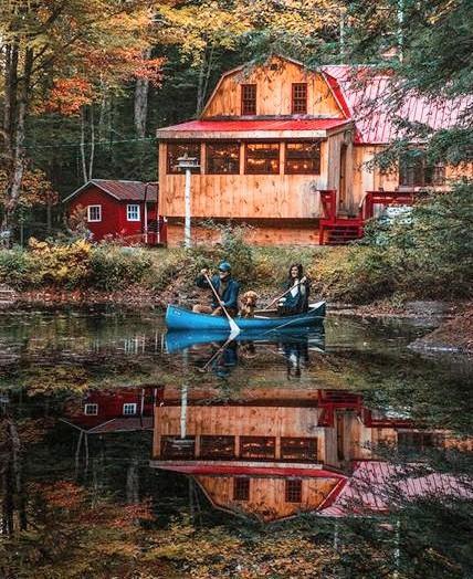 A rustic house near a beautiful lake with autumn leaves on the trees!*& all this reflecting in the stillness of the lake as a blue canoe with people and a dog slowly paddle in the lake 