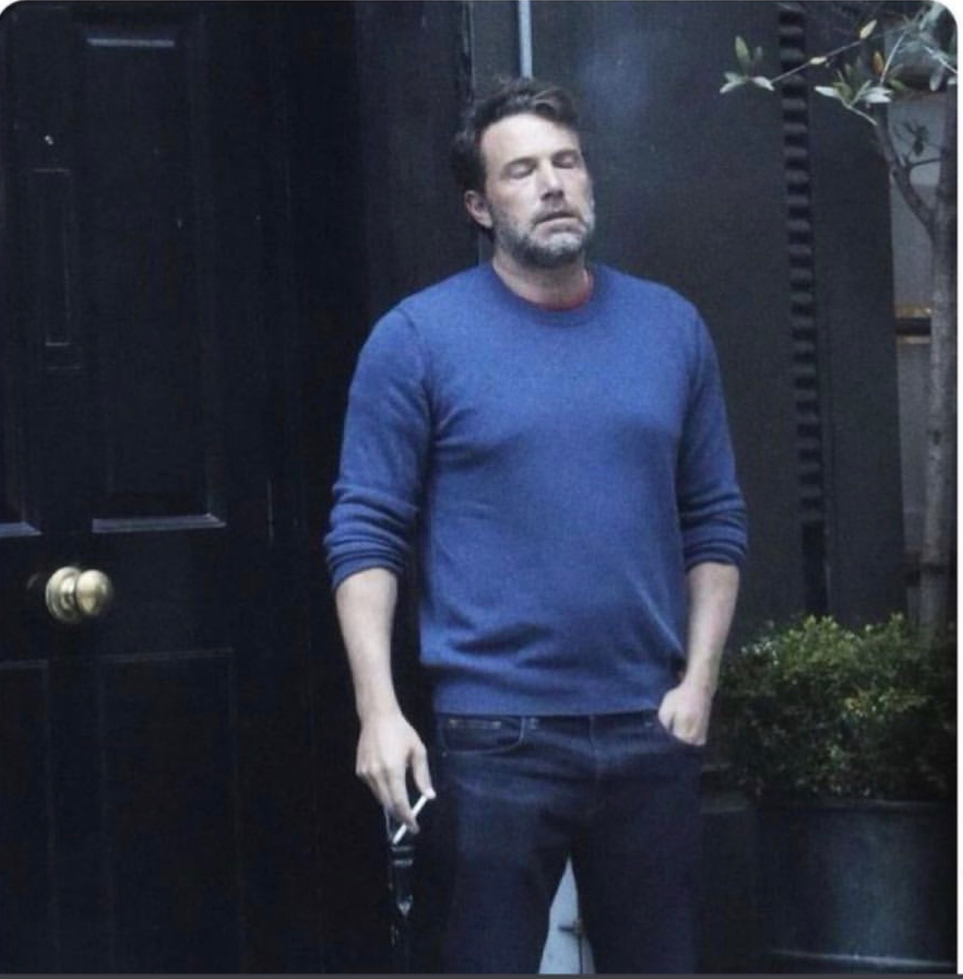 Ben Affleck, standing outside with a cigarette. His eyes are closed, face pointed upwards. He looks tired like the weight of the world is on his shoulders