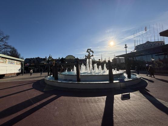 The Fountain of Friendship by the park entrance; the sun still sits low in the blue sky, throwing long shadows across the ground.