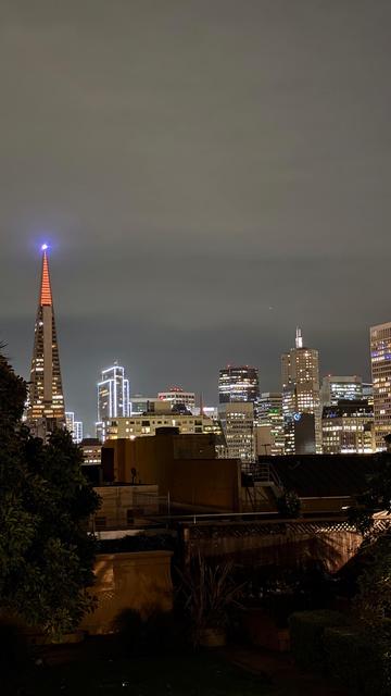 View east towards the financial district from Nob Hill, San Francisco - thr Transamerica pyramid is lit up orange at the top of the pyramid and the Embarcadero Center buildings have holiday lights on the edges.