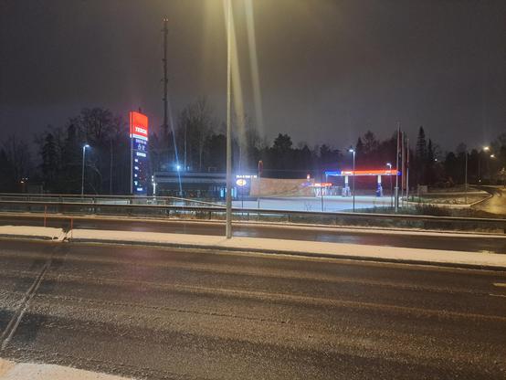 Aamuhämärässä otettu kuva Teboil-kylmäasemasta. Hintapylväs näyttää tyhjää.
Aseman pihalla Rolls-drivein.
Etualalla loskassa märkä katu. Asfaltin ulkopuolella lunta. Kadut ja pihat valaistu.