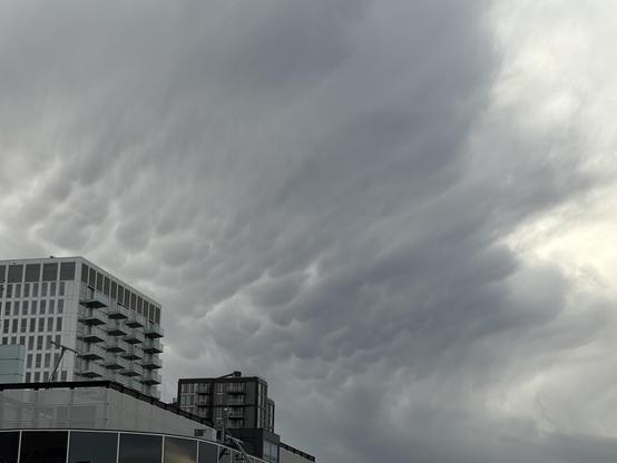 Een grijze wolk met een soort hangende bolvormige uitstulpsels onderaan. Aan de onderkant van de foto nog de bovenkant van gebouwen.