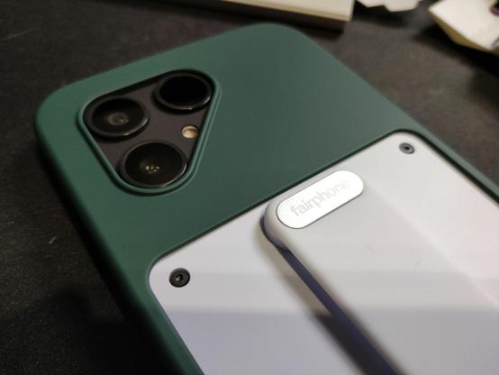 A black Fairphone 6 with a white fingerprint installed and a green plastic/rubber cover.