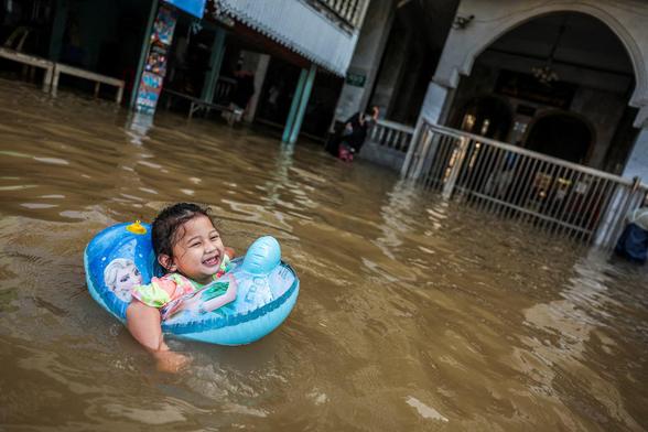 Duha, 2, plays on a polluted flooded road in an inflatable.