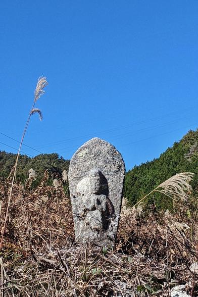 真っ青な空を背に枯れた草むらに佇む馬頭観音像の写真