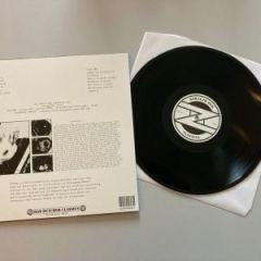 Eine Vinylplatte, die neben ihrer Hülle ausgestellt ist, auf deren einer Seite Text und Bilder zu sehen sind. Die Platte ist schwarz und hat ein Etikett in der Mitte.