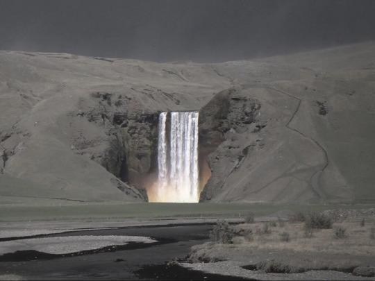 Waterfall in Iceland amidst a mountain covered in ash after the Reykjanes volcano eruption.