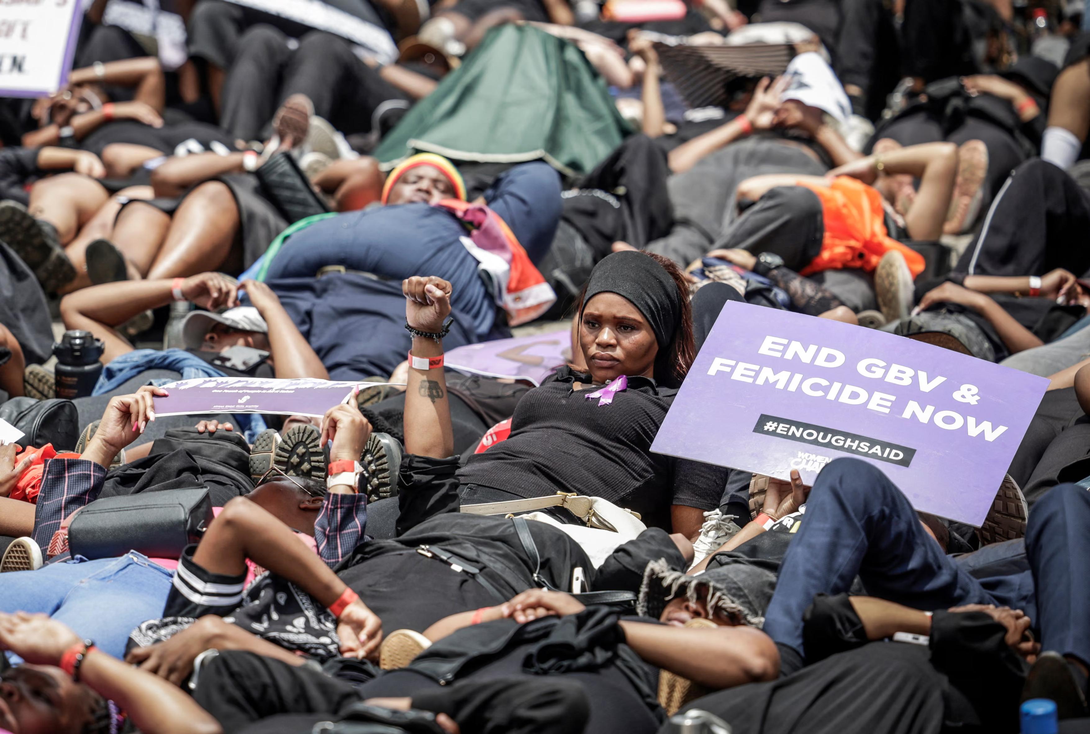Women lie on the ground during the Women’s Nationwide Shutdown. One holds a placard which reads:
END GBV & FEMICIDE NOW