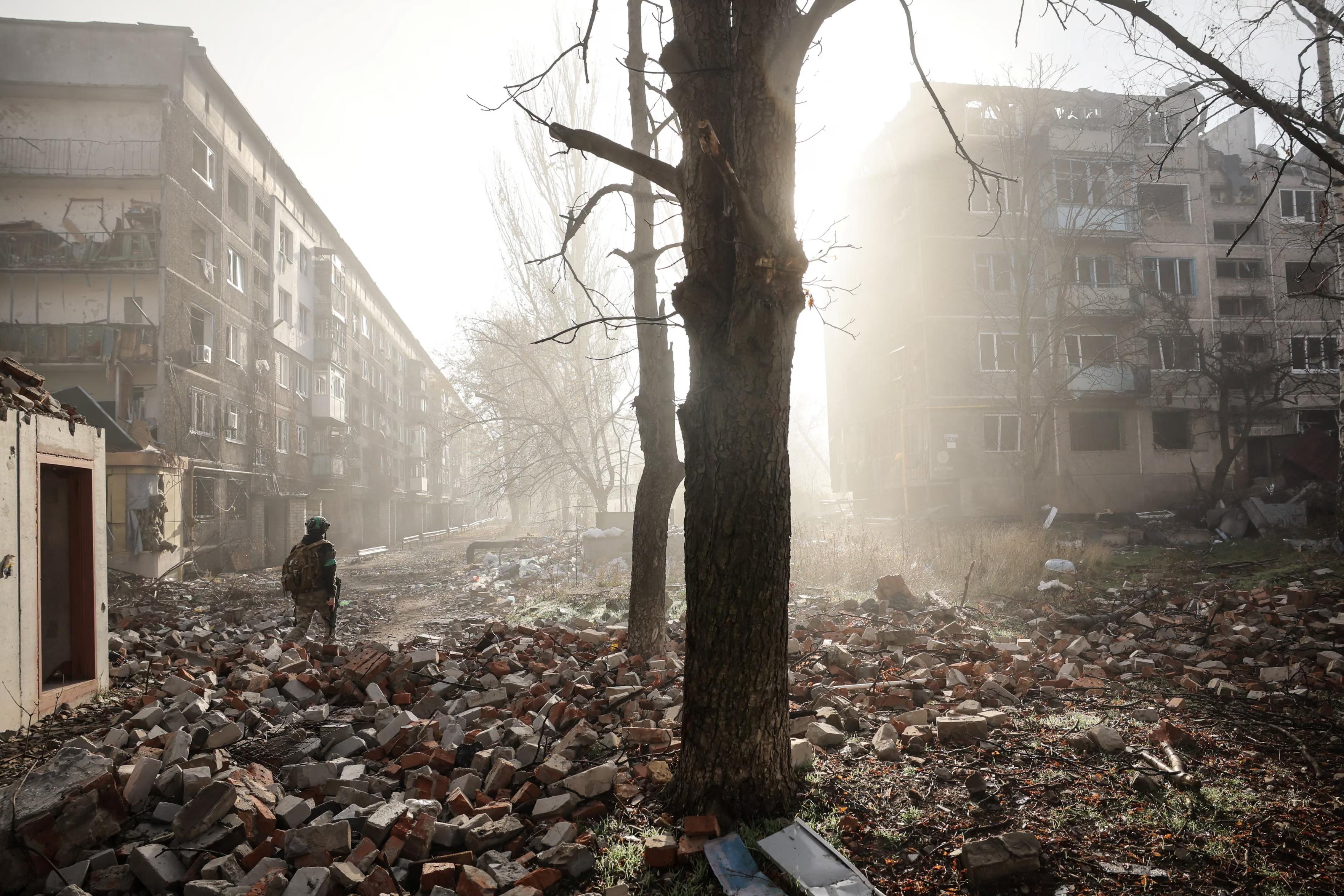 A Ukrainian serviceman walks near apartment buildings damaged by a Russian military strike.