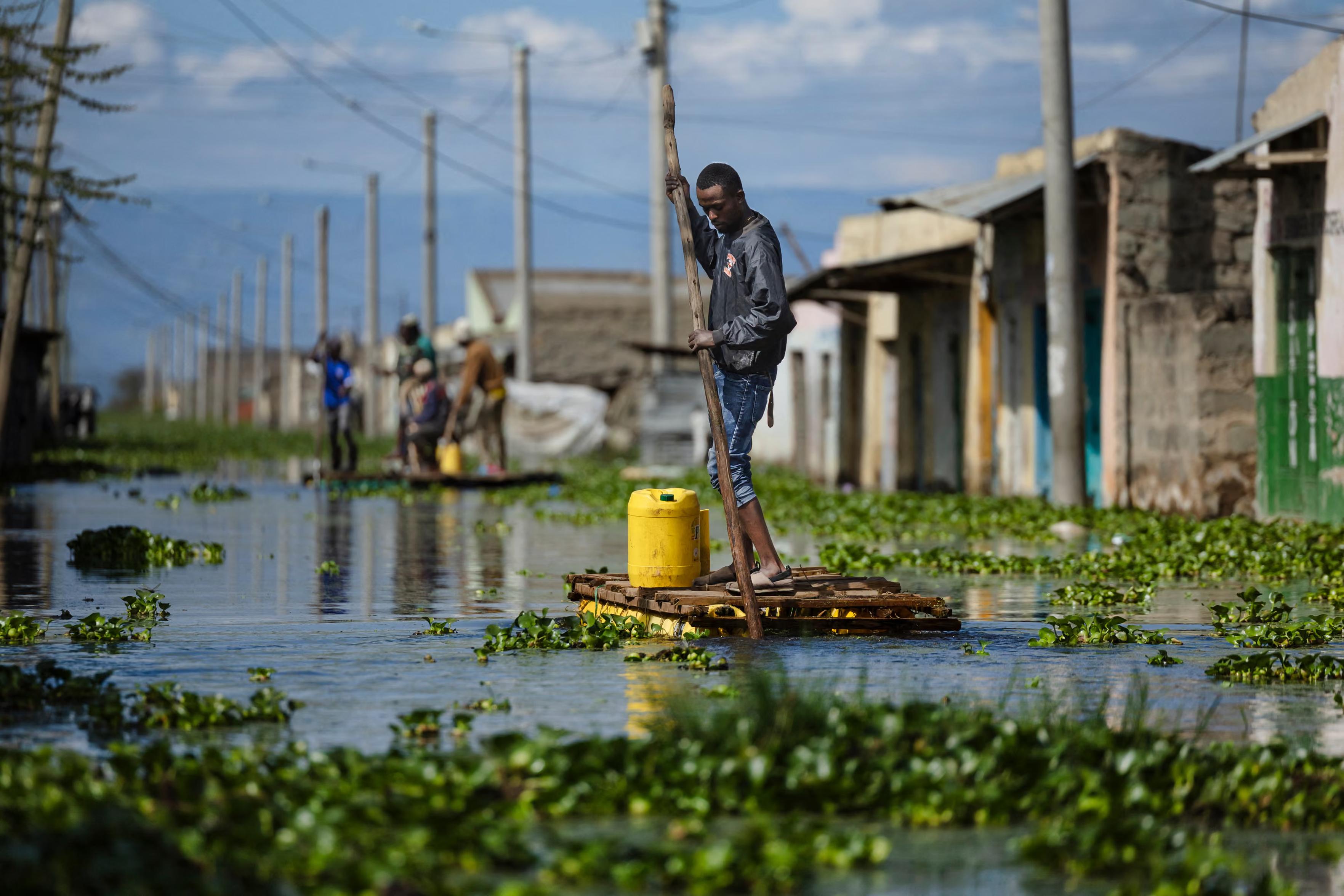 Residents manoeuvre makeshift rafts with water containers over a flooded access road to their residential blocks.