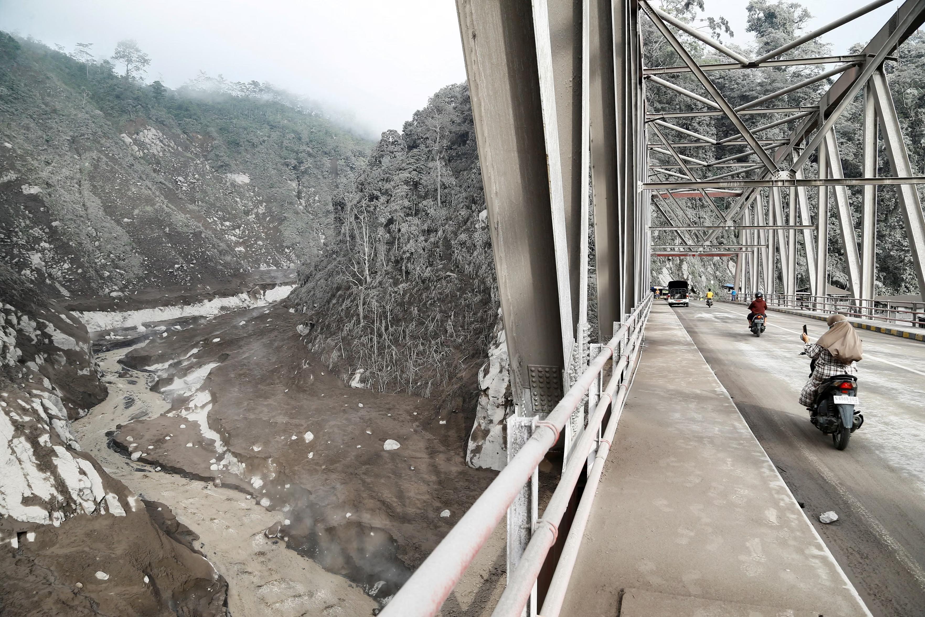 People ride past an area covered with volcanic ash after the eruption of Mount Semeru.