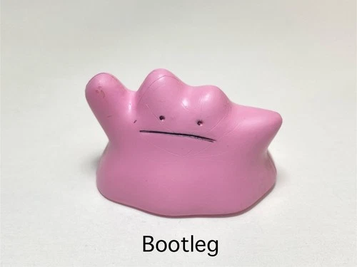 A picture of a slightly off looking figure of the Pokémon "Ditto". It is a pink blob with two small, black dots for eyes and a small black line for a mouth, forming a sort of neutral and disinterested expression. It is sitting on a plain white surface and text has been added digitally to the image, below the figure. The text is plain, black, sans-serif, and simply reads "Bootleg".