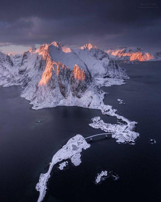 An aerial view of Norway, with the mountaintops lit up by rising sun.