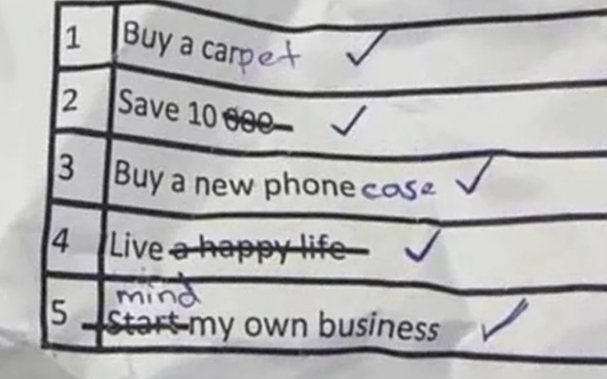 Close-up of a handwritten checklist on lined paper, listing five goals with checkmarks next to four. 

The goals: 
"Buy a car" 
"Save 10,000," 
"Buy a new phone" 
"Live a happy life,"
"Start my own business".

The goals are edited by hand and read as:
"Buy a carPET," 
"Save 10" 
"Buy a new phone CASE," 
"Live"
"Mind my own business"

Every Item is checked.
