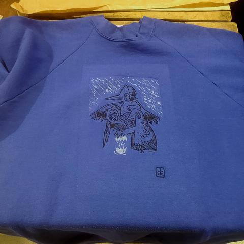 Pull bleu foncé, impression en noir et blanc : des oiseaux sous la neige regardent l'un d'eux qui a cassé un oeuf, dans lequel il y a... de la neige. Eh oui.