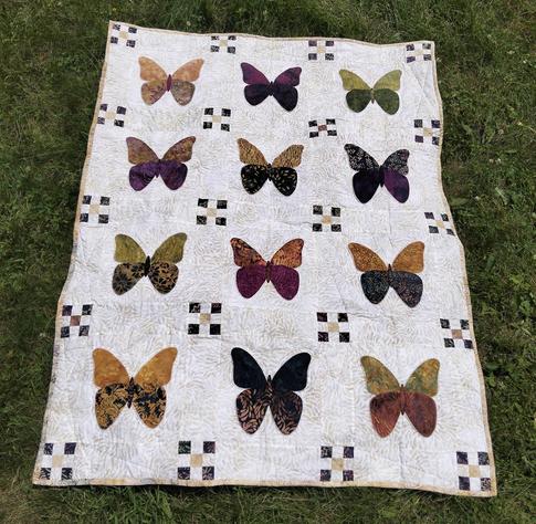 a quilt, it is 12 butterflies in rows of three against a white background, each in a separate window, a nine patch at each corner of the windows 