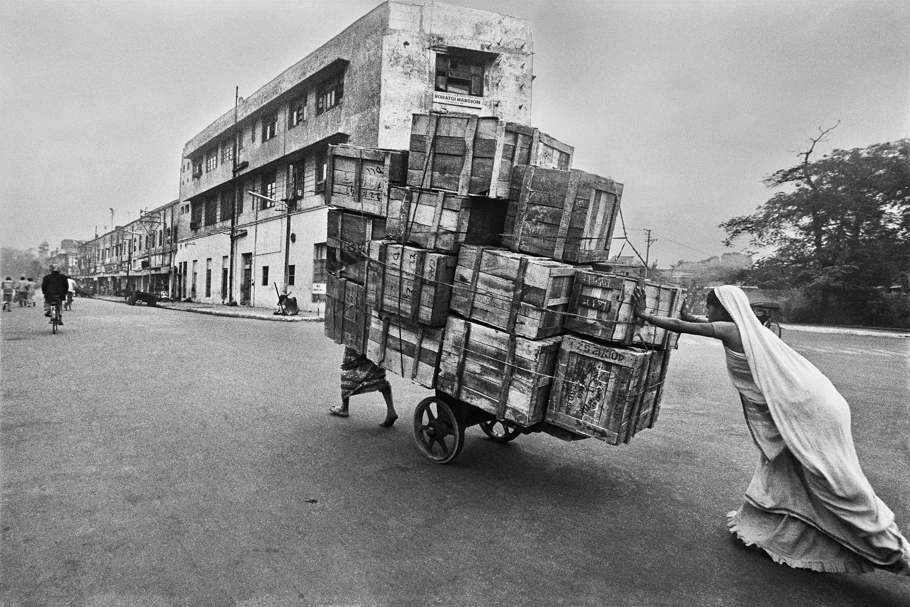 A black and white image of two women pulling and pushing a card overloaded with wooden crates.
