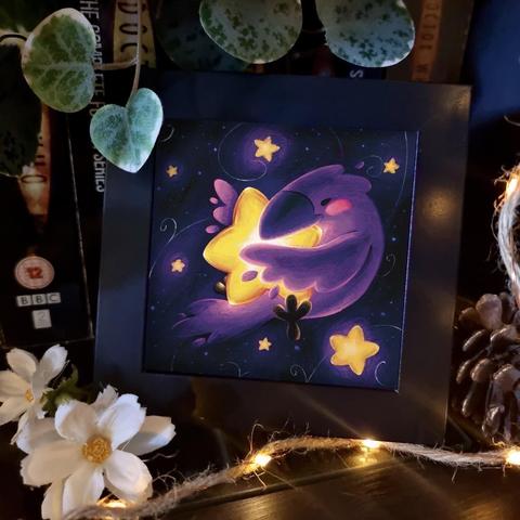 A picture of an illustration in a small black frame, surrounded with fairy lights, flowers and plants.
It is a square digital illustration of a purple raven floating in space and surrounded with bright stars. It is keeping the biggest one safe between its wings, its body curled up around it. A sense of warmth and safety emanating from the scene. 