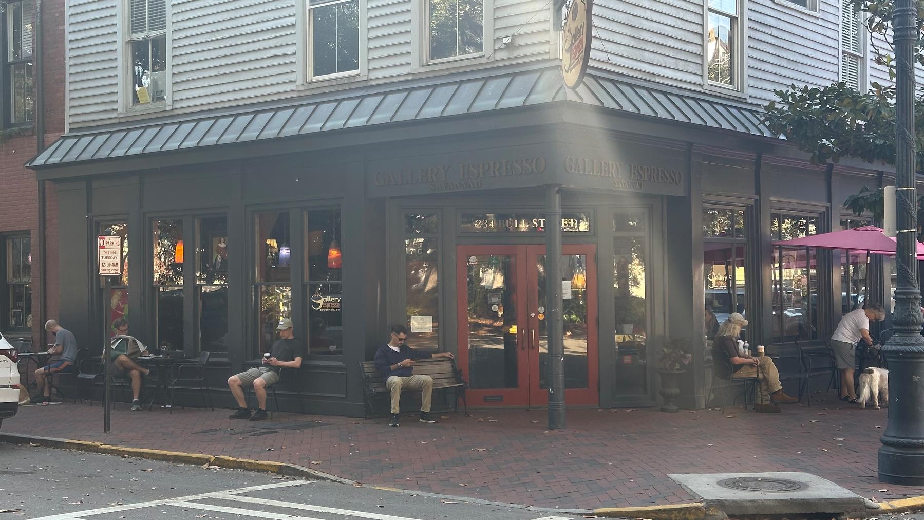 Exterior shot of coffee shop building. There are people lining the outside, sitting, reading 