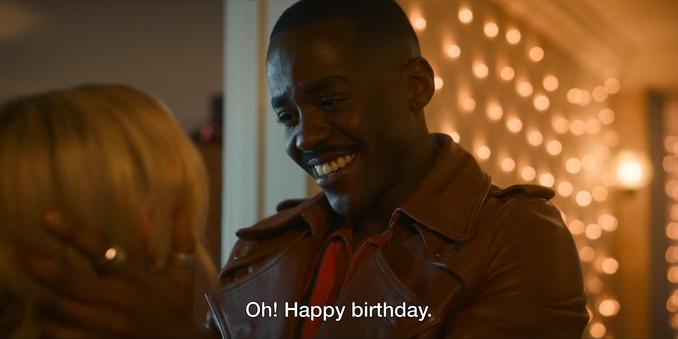 Ncuti Gatwa episode. The Doctor is in Ruby’s apartment with her mum. Lights line the hallway. The Doctor is in his iconic outfit of the orange jumper and long leather pea coat. He’s grinning a wide smile, squeezing Ruby’s face, and says, “Oh! Happy birthday.”