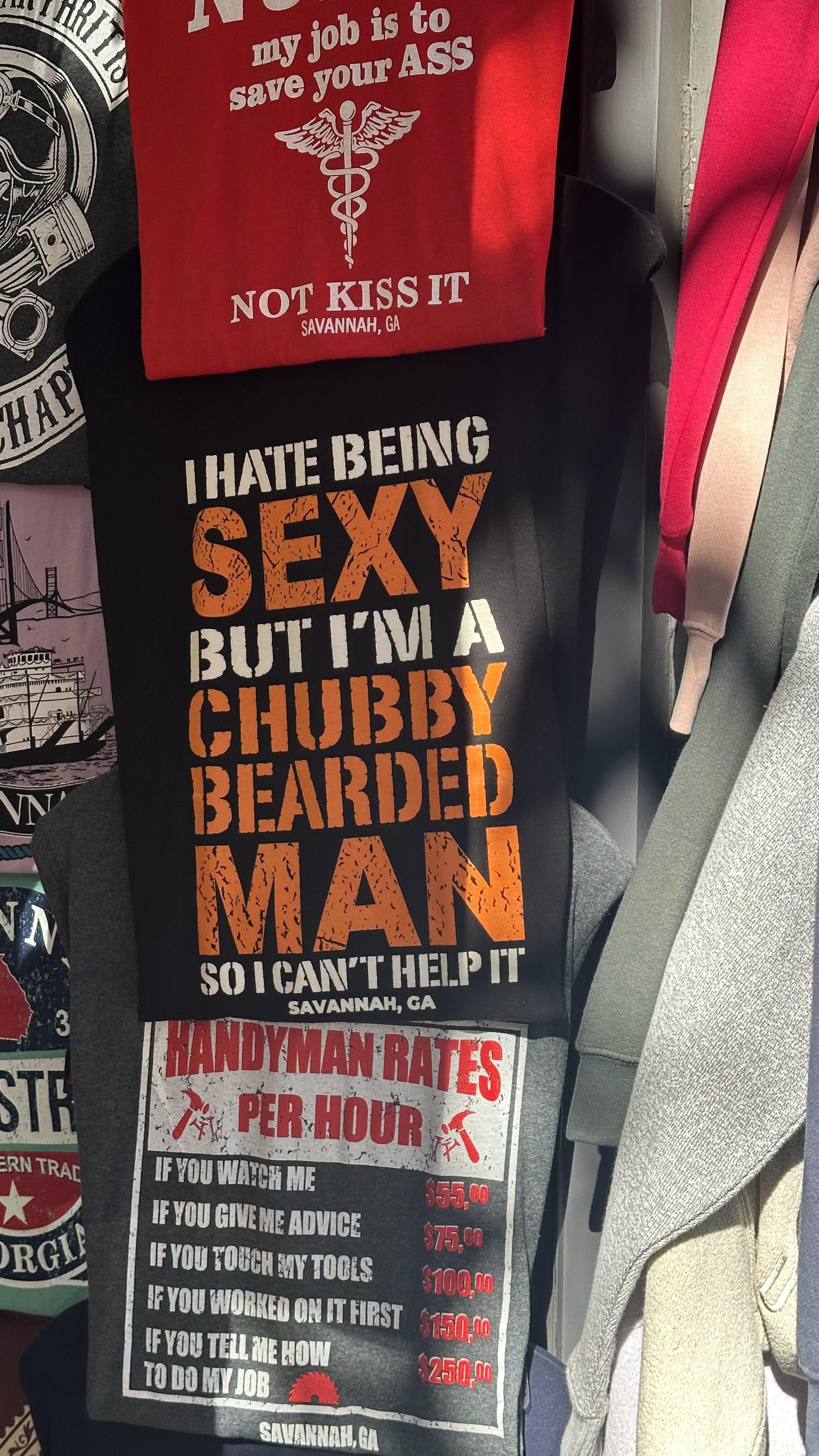 Image of t-shirt displayed for sale, black with orange text stating, "I HATE BEING SEXY BUT I'M A CHUBBY BEARDED MAN SO I CAN'T HELP IT," 
