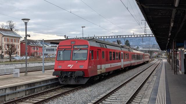 A trainset consisting of a CJ class RBDe 567 motor coach with a low-floor intermediate and a control car is waiting on its departure at Porrentruy. The livery is red with a white horizontal strip underneath the windows and white doors. A drawn horse consisting of white contours is displayed underneath the driver window.