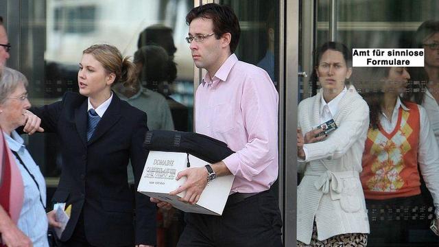 Menschen, die aus einer Drehtür kommen, mutmaßllich ein Bürogebäude; sie wirken emotional, ein Mann mit Oberhemd trägt einen kleinen Pappkarton, darauf eine Laptoptasche