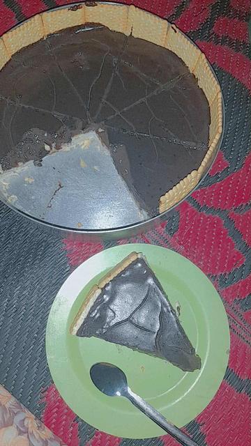 Cononut pie with a biscuit crust, partly sliced, next to a green plate with a piece of the pie and a spoon, on a patterned red and gray surface.